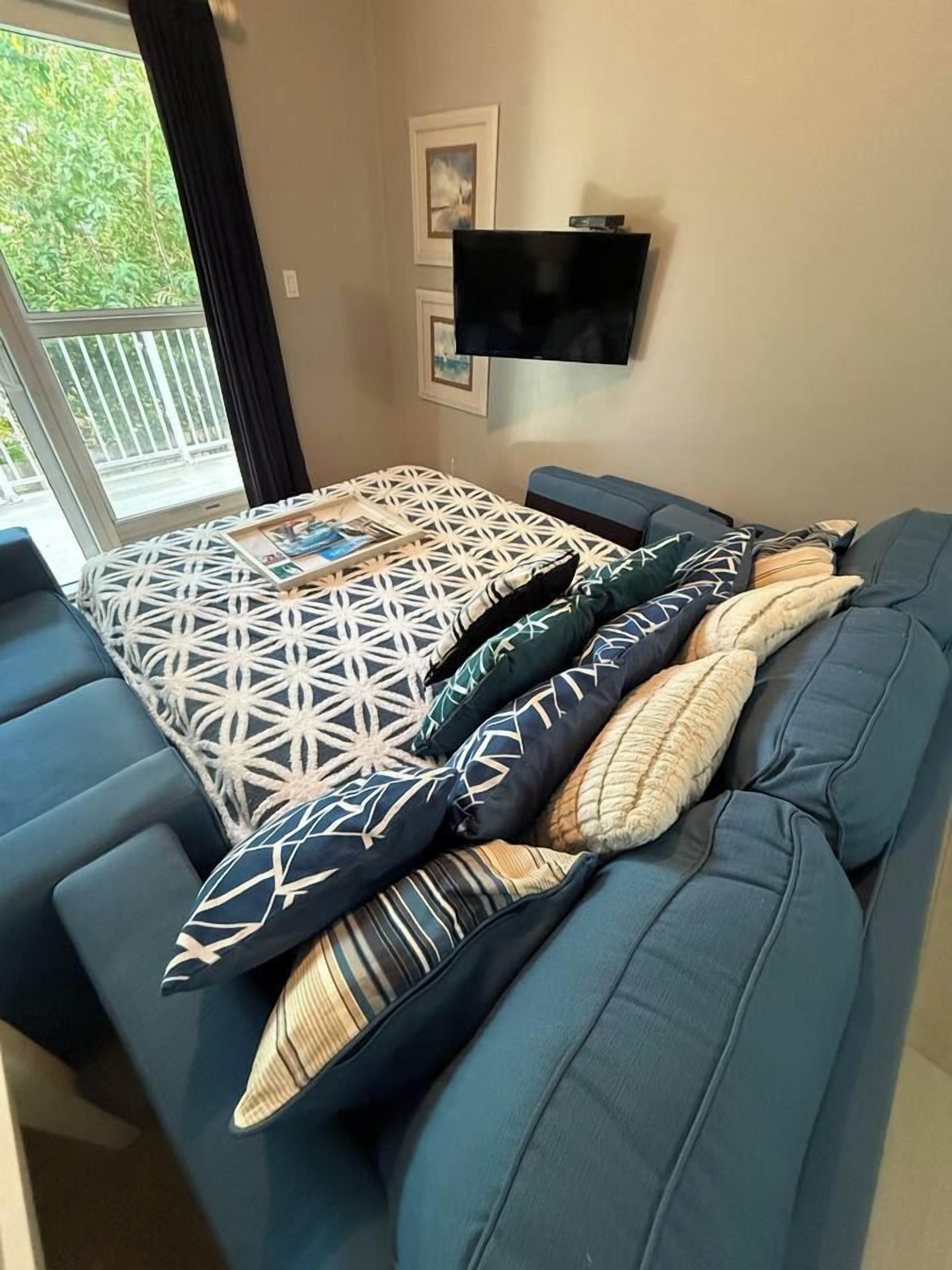 A room with a sofa bed, a flat-screen TV mounted on the wall, and a window with a view of greenery.