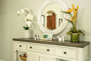 Een dressoir met een spiegel, een vaas met witte bloemen, een kamerplant en een kaart met een familiedesign.