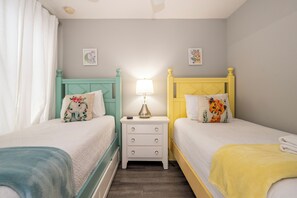 A twin room with two beds, each with a distinct headboard color, a bedside table with a lamp, and two wall-mounted pictures. - Cozy 5BR Pool Home Mario Game Room Near Disney (Kissimmee)