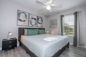 A bedroom with a bed, a nightstand, a desk lamp, a ceiling fan, and artwork on the wall. - Near Disney Private Pool & Harry Potter Room (Kissimmee)