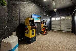 A room with arcade machines, a television, and a garage door. - Near Disney Pool Home with Minions & Mickey Rooms (Kissimmee)