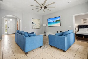 Un salon avec deux canapés, un ventilateur de plafond et un grand écran de télévision.