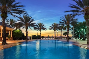 A swimming pool with palm trees, lounge chairs, and a building in the background. - Near Disney 3BR Reunion Resort Condo Pets Welcome (Kissimmee)