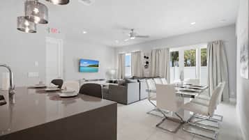Habitación de hotel moderna con comedor, sofá, televisor y vistas al exterior.