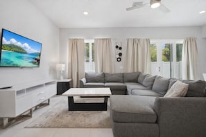 A modern living room with a sectional sofa, a flat-screen TV, and a dining table. - Near Disney 3BR Reunion Resort Condo Pets Welcome (Kissimmee)