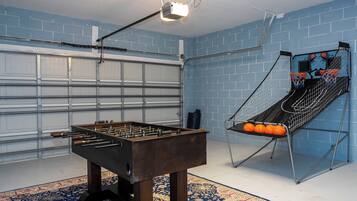 Una stanza con un tavolo da ping pong, un canestro da basket e un portone da garage.