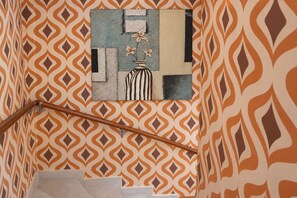 Un escalier avec un mur décoré de motifs et un tableau représentant un vase de fleurs.