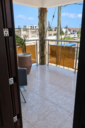 Un balcon donnant sur des immeubles et le tronc d’un arbre.