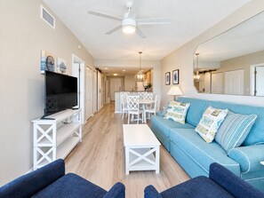 Ein Wohnzimmer mit Fernseher, weißen Möbeln, einem blauen Sofa und einem Deckenventilator.