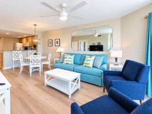 A modern living room with a sofa, chairs, a coffee table, and a dining area with chairs and a table. - Wake Up on the Gulf - Resort Life Beach Pool & Spa (Treasure Island)