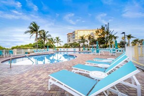 A pool area with lounge chairs and a building in the background. - Wake Up on the Gulf - Resort Life Beach Pool & Spa (Treasure Island)