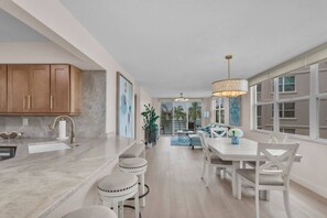 A modern kitchen with a marble countertop, wooden cabinets, and a dining area with a white table and chairs. - Bayfront Condo Big Views Private Beach & Pool (St. Petersburg)