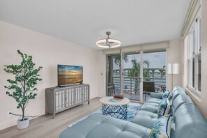 A modern living room with a sofa, a television, a cabinet, and a view of a bridge and water. - Bayfront Condo Big Views Private Beach & Pool (St. Petersburg)