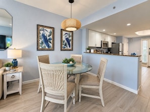 A dining area with a round glass table, wicker chairs, and a hanging light fixture. - Salt Air, Pool @ Sunset Vistas in Treasure Island (Treasure Island)