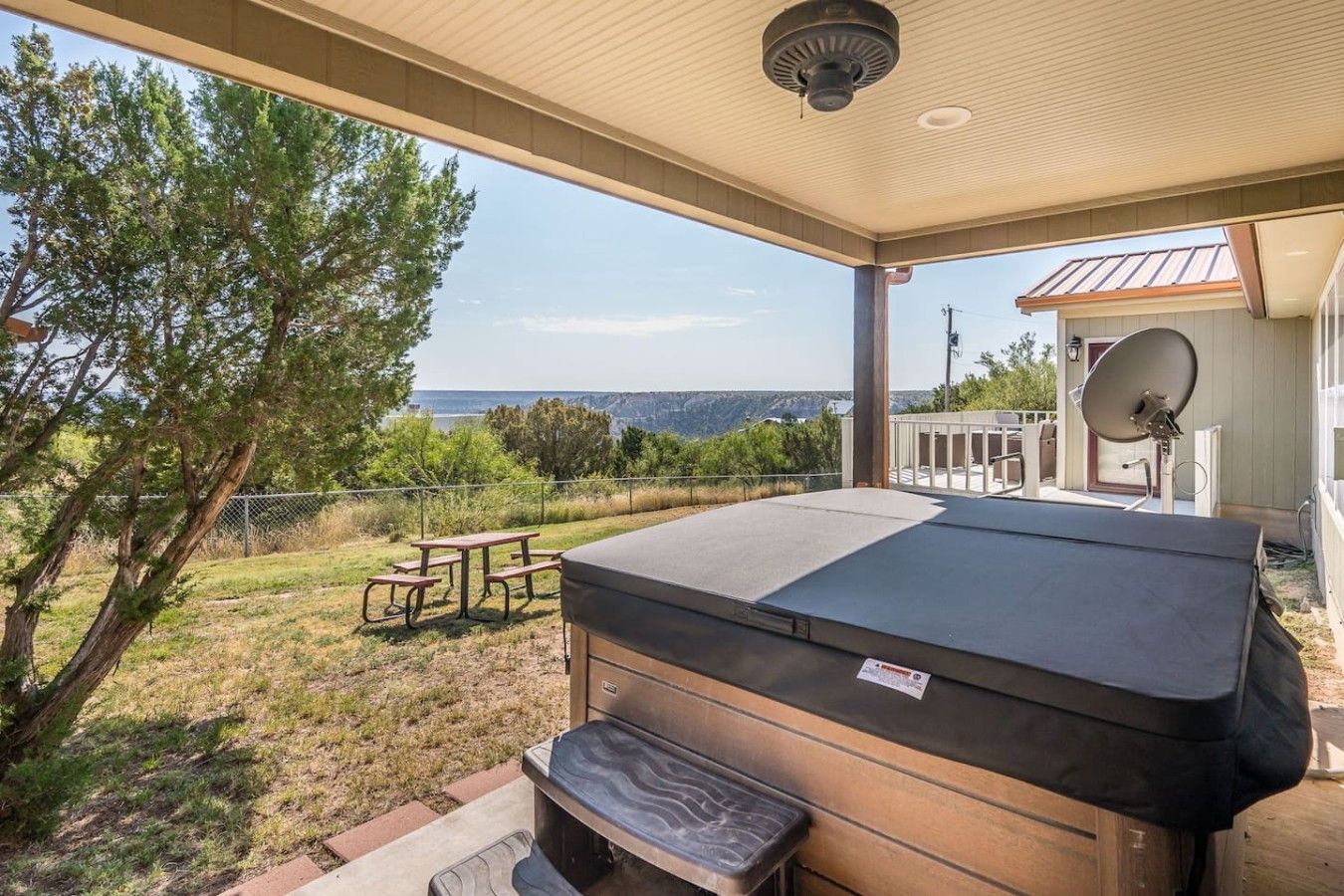 A covered patio with a hot tub, picnic table, and a view of the landscape.