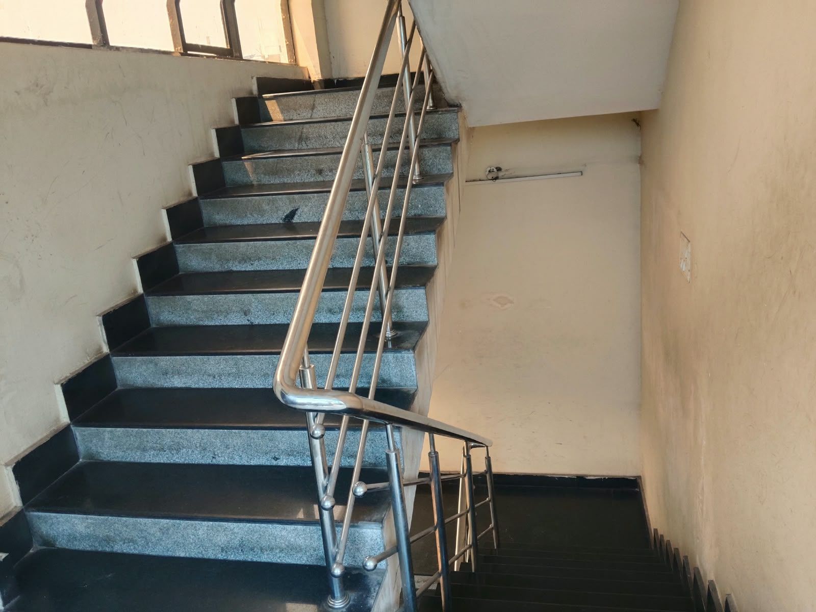 Una escalera con barandas metálicas y una baranda en el lado izquierdo, que conduce a un piso superior.