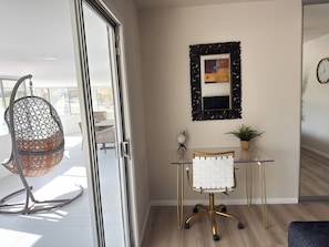 Ett modernt kontorsutrymme med ett skrivbord i glas, en vit kontorsstol, en dekorativ spegel och en hängstol.