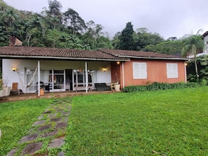 A house with a tiled roof, a porch with seating, and a grassy yard. - Casa Paz (Teresópolis)