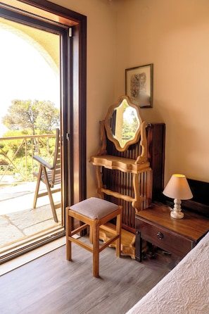 A room with a wooden chair, a dresser, a mirror, and a lamp. There is a door leading to an outdoor area with a view of trees. - Villa Dryas a traditional private pool villa,in the riviera of Attica,Lagonisi (Kalivia Thorikou)