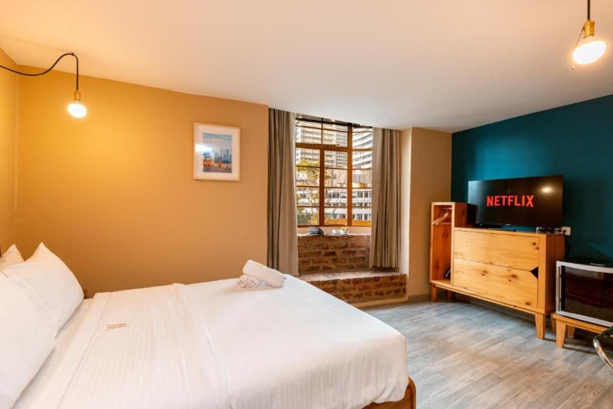 Ein Hotelzimmer mit Bett, Fernseher, Schreibtisch und einem Fenster mit Vorhängen.