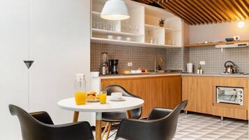 A modern kitchen with a dining area, featuring a round table with chairs, a built-in oven, and a coffee maker.