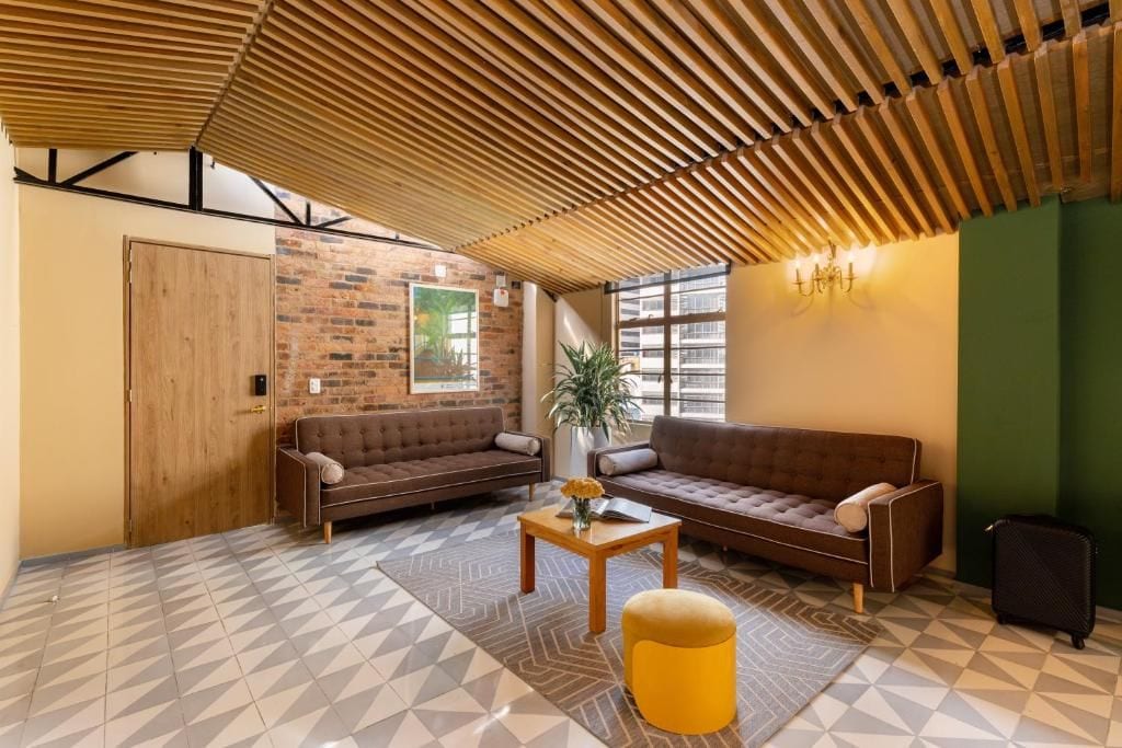 A modern lounge area with a brick wall, two sofas, a wooden ceiling, and a patterned floor.