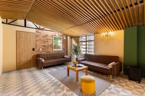 A modern lounge area with a brick wall, two sofas, a wooden ceiling, and a patterned floor. - Casa Avenida Jimenez (Bogotá)