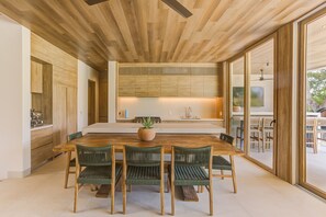 A modern kitchen with wooden cabinetry, a central island, and a dining area with a wooden table and chairs. - Luxury Villa in El Tigre with Beach Club (Nuevo Nayarit)