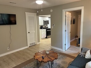 A living room with a round wooden coffee table, a flat-screen TV mounted on the wall, and a sofa.