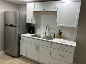 A modern kitchen with white cabinets, a stainless steel refrigerator, a sink, and a coffee maker. - Perfect place to put up your feet while enjoying Husker activities. (Lincoln)