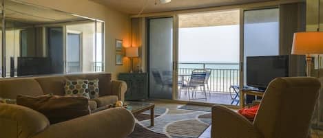 A hotel room with a sofa, armchairs, a television, a balcony with a view, and a ceiling fan.