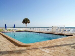 A rectangular pool with a wooden deck surrounding it, a palm tree, and a view of the ocean. - East Wind #3030 Oceanfront Traffic Free Beach 2/2 (Ponce Inlet)