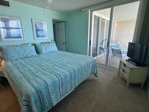 A bedroom with a bed, a television, and a sliding glass door leading to a balcony. - East Wind #3030 Oceanfront Traffic Free Beach 2/2 (Ponce Inlet)