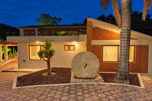 A modern house with a brick facade, a stone sculpture in the front, and a palm tree. - Vrbo Property (Oaxaca de Juárez)