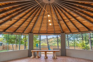 A covered outdoor area with a wooden ceiling, a table, and large windows offering a view of the surrounding landscape.