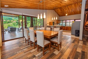 A spacious dining area with a wooden table and chairs, a kitchen in the background, and a view of greenery outside. - Vrbo Property (Oaxaca de Juárez)