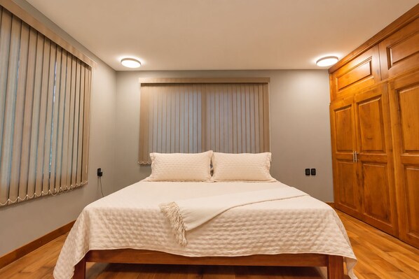 A bedroom with a bed, wooden wardrobe, and a window with blinds. - Vrbo Property (Oaxaca de Juárez)