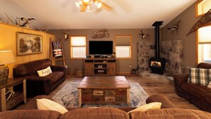 A cozy living room with a fireplace, a television, and rustic decor. - Hunters Haven - In Town - WiFi - Lounge/Game Room - Grill - Washer/Dryer (Red River)