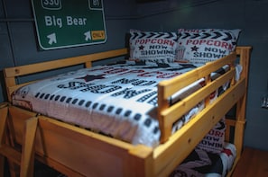 Ein hölzernes Bett mit einer Steppdecke im Filmstreifen-Design, Kissen mit Popcorn und kinobezogenen Texten, sowie ein grünes Hinweisschild darüber.