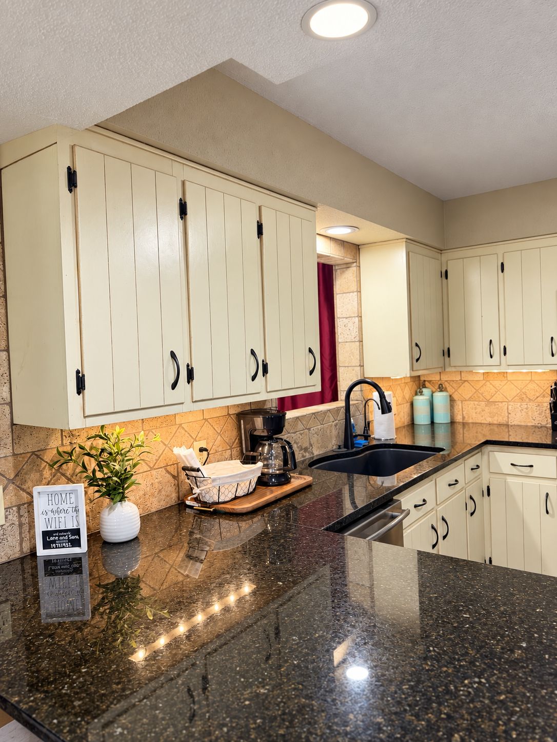 A kitchen with beige cabinets, a granite countertop, a coffee maker, and a sign on the counter.