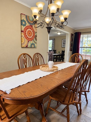 A dining room with a wooden table, chairs, a chandelier, and a decorative wall piece. - (Many)