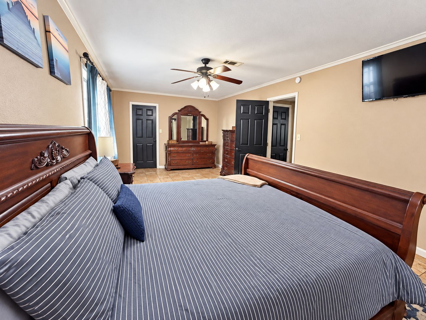 A bedroom with a large bed, a dresser, a mirror, and a ceiling fan.