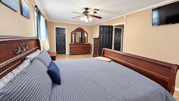 A bedroom with a large bed, a dresser, a mirror, and a ceiling fan.