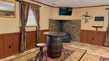 A room with a stone fireplace, a round wooden barrel, a small stool, a television mounted on the wall, and a patterned rug on the floor.