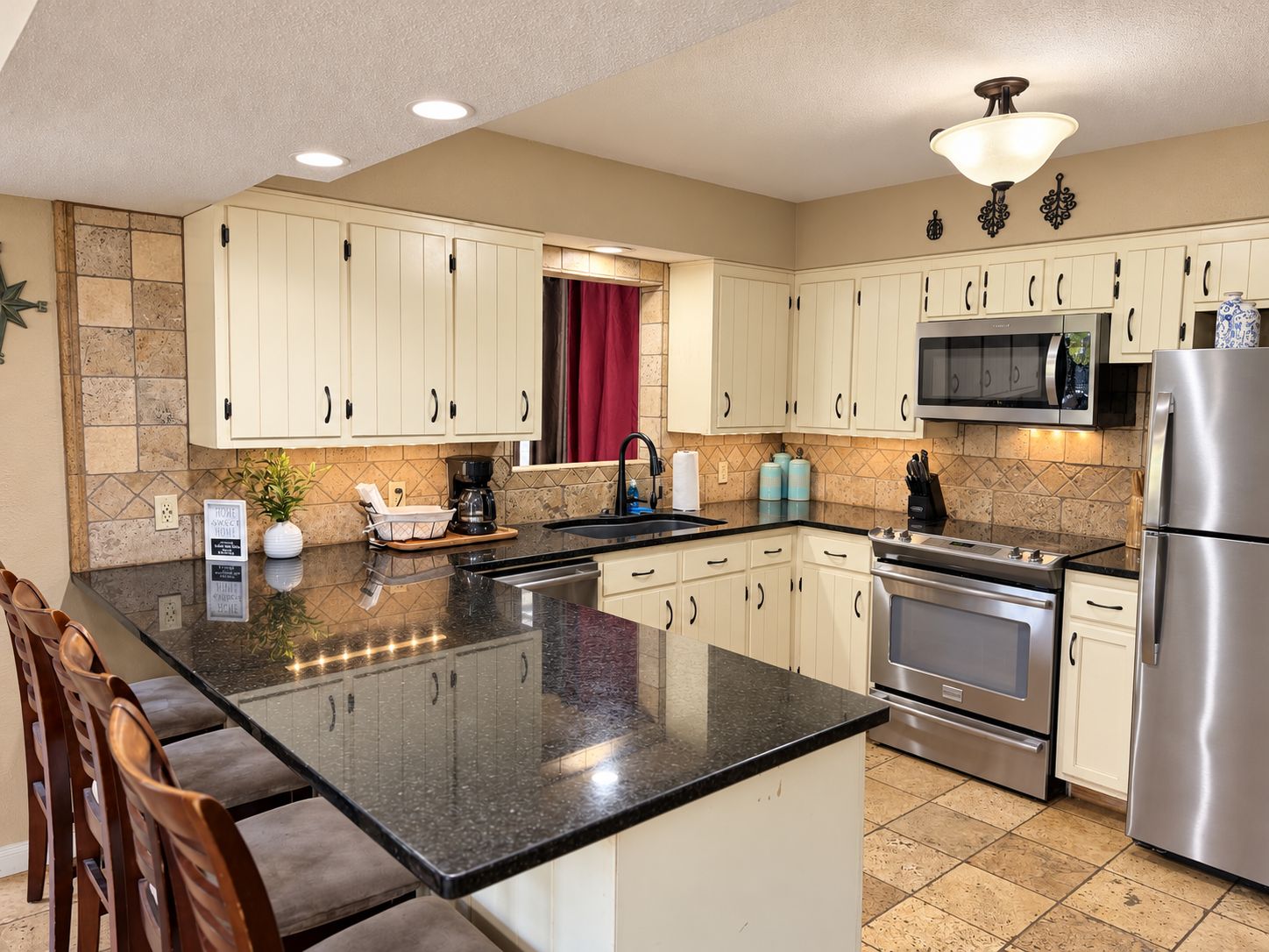 A modern kitchen with white cabinets, a granite countertop, stainless steel appliances, and a red curtain.