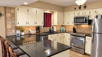 A modern kitchen with white cabinets, a granite countertop, stainless steel appliances, and a red curtain.