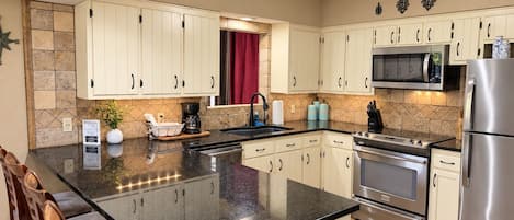Cozinha moderna com armários brancos, bancada de granito, eletrodomésticos de aço inoxidável e cortina vermelha.