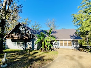 A two-story house with a balcony, a garage, and a large tree in the front yard. - (Many)