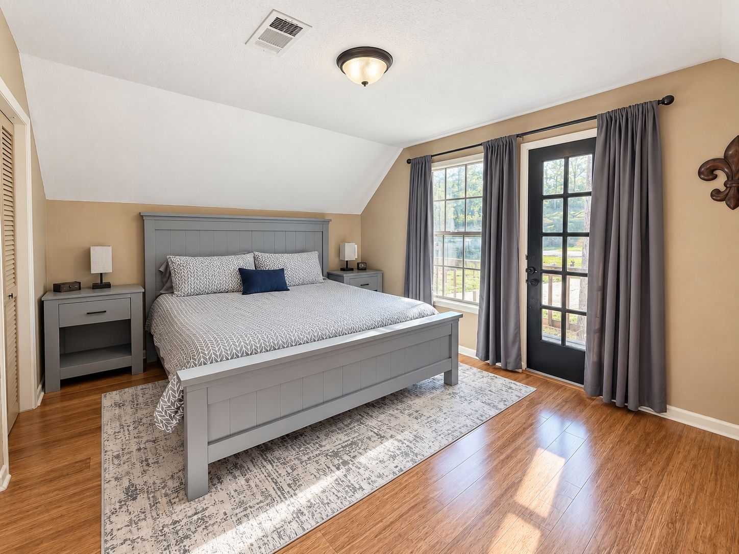 A bedroom with a bed, nightstands, a window with curtains, and a door.