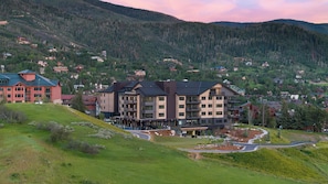 Ein mehrstöckiges Hotel im modernen Stil, auf einem Hügel mit Blick auf einen bewaldeten Bergrücken.